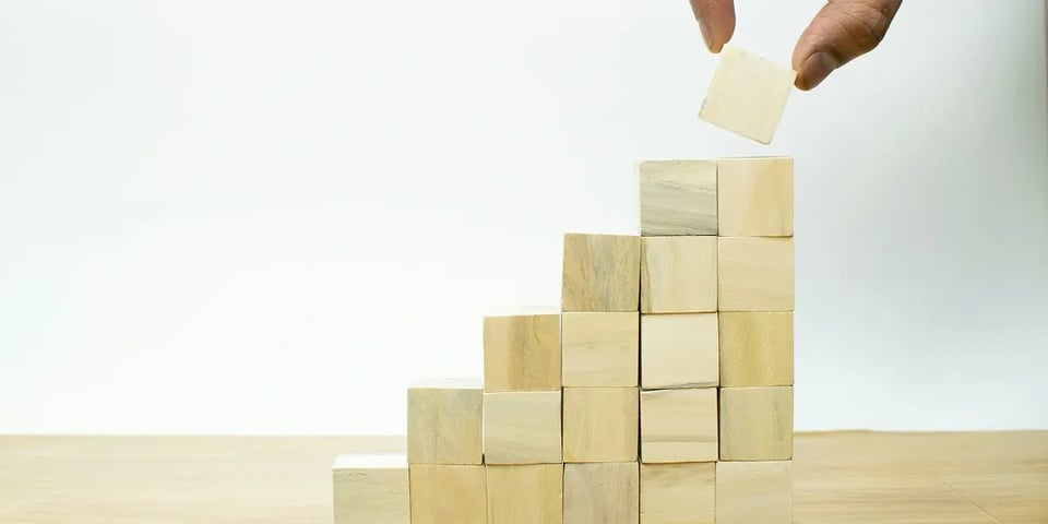 A hand stacks wooden cube blocks in a stair formation