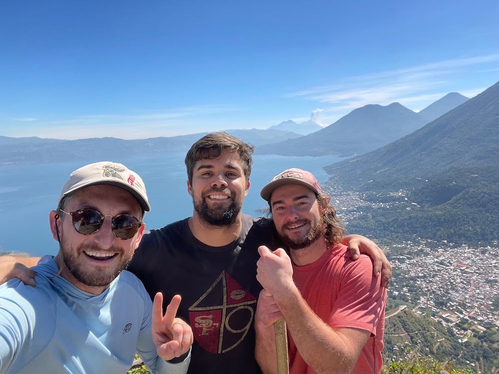 Two digital foundry software consultants and a digital foundry software engineer stand on a trail overlooking Lake Atitlan and lakeside villages in Guatemala