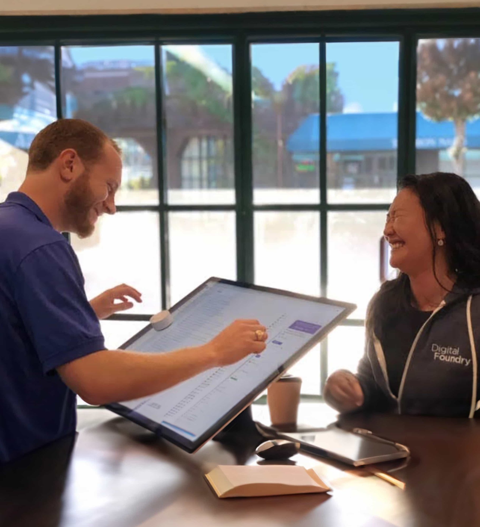 Two smiling employees working on a large touch-screen